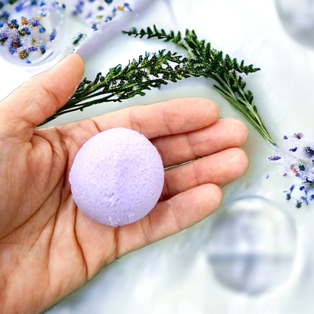 Bomba efervescente de lavanda sostenida por una mano que está sobre el agua